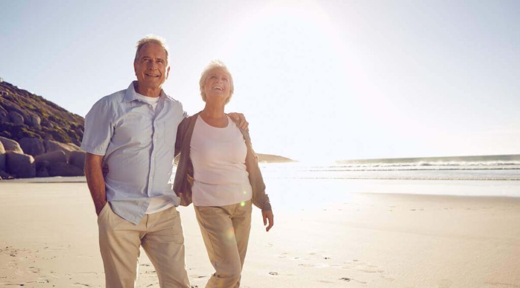 Senior couple walking on the beach discussing "will I have enough money to retire"